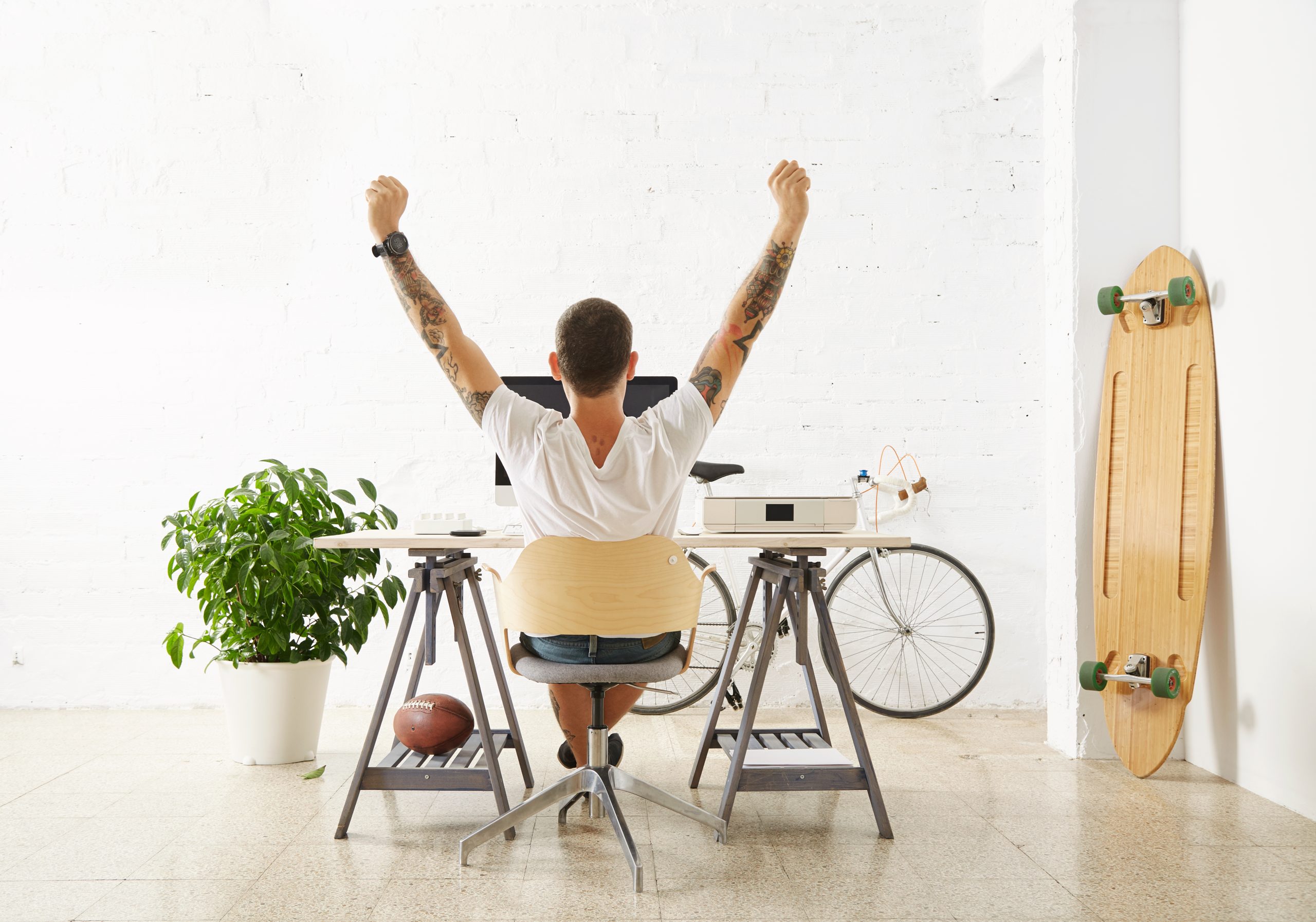 lucky freelancer front his hybrid work environment with his hobby toys longboard vintage bicycle green plant stretching his hand air while making break scaled